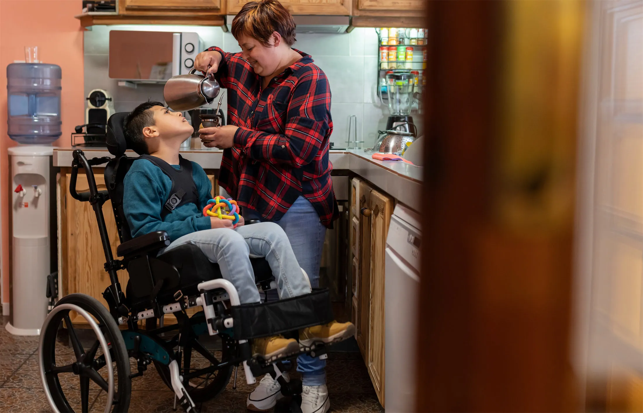 Photo of woman and child in a kitchen. Child is in a wheelchair and the woman is pouring coffee and smling